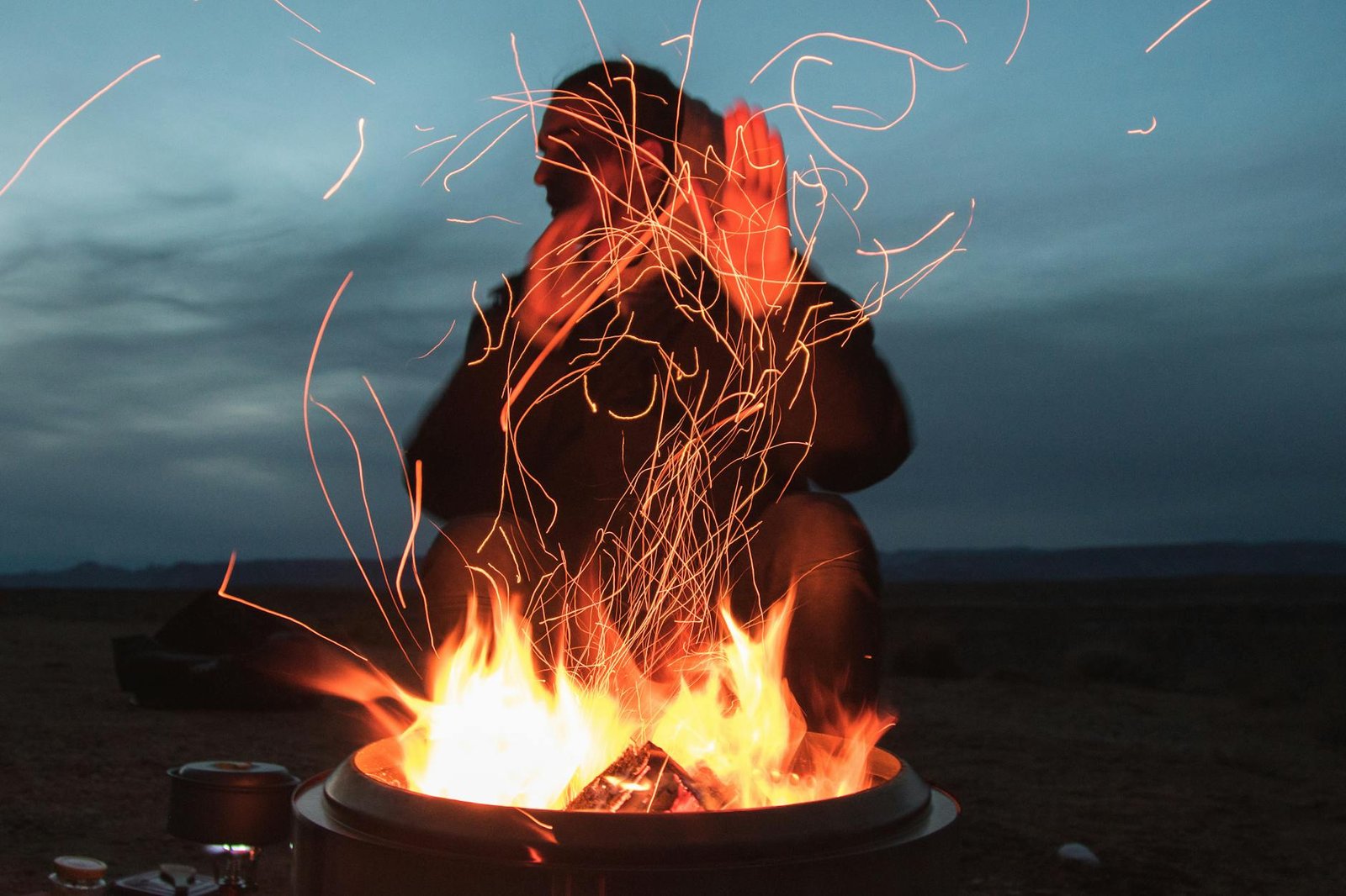 Man sitting facing fire in pot during night