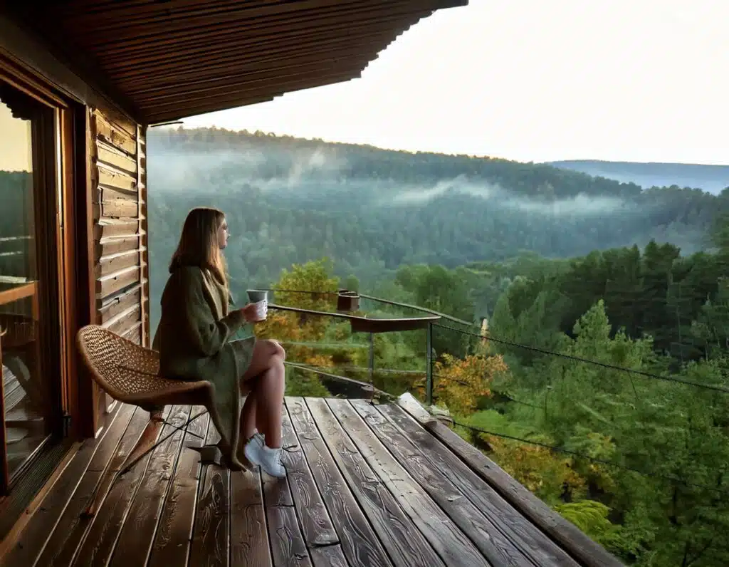 A woman sitting on a porch with a view of the mountains while tiny cabin living in ohio
